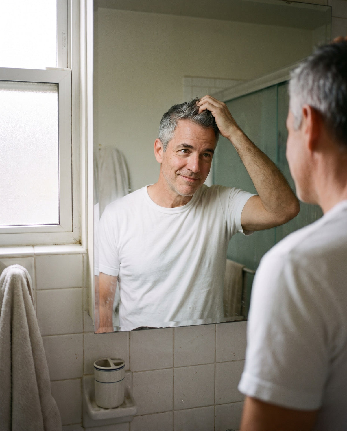 Man with thick grey hair checking his hair in the bathroom mirror